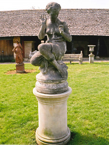 A 19th Century composition statue of a maiden seated on a rock, mounted on a solid limestone drum pedestal.